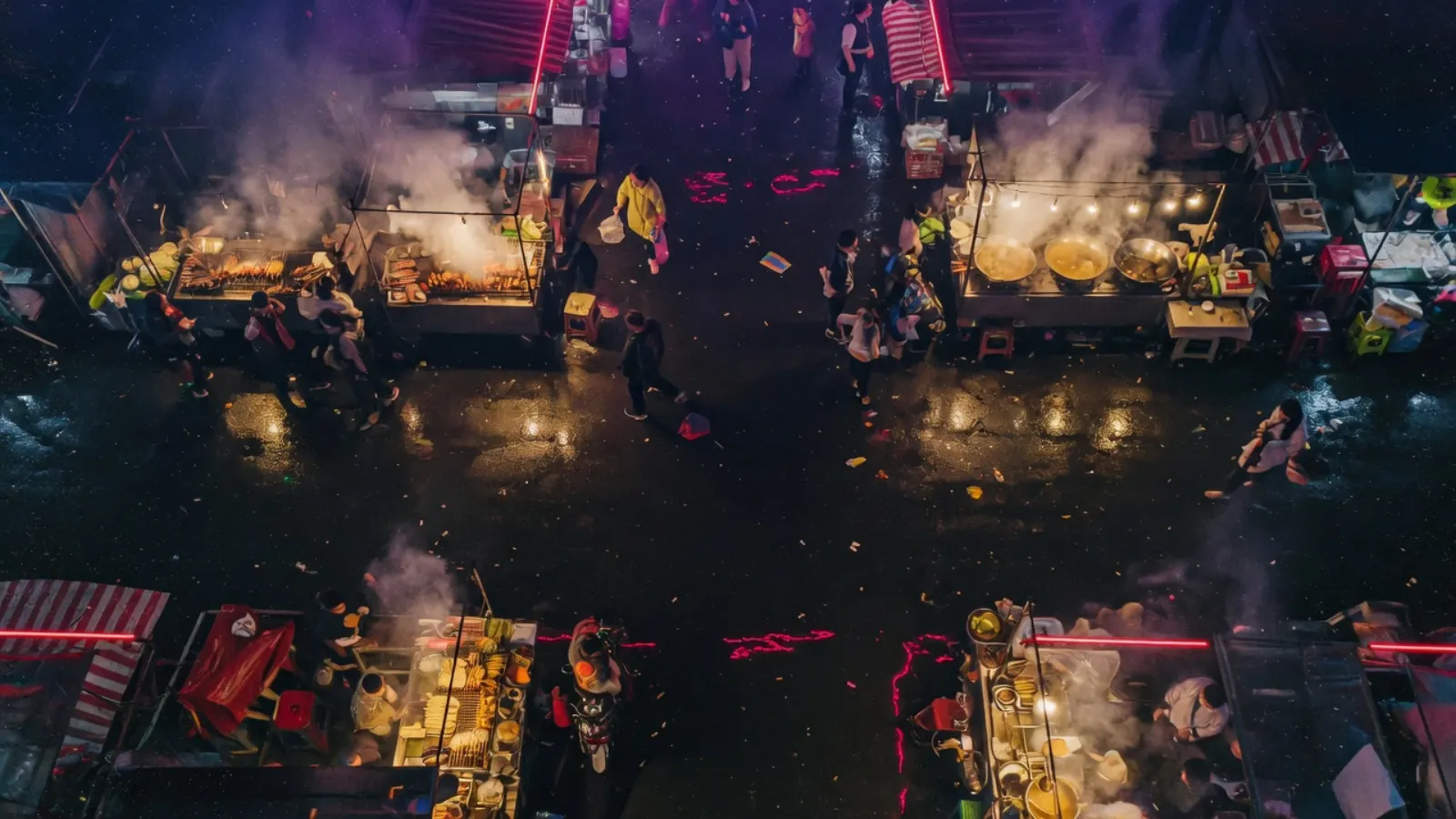 雨后俯视夜市：摊位钨丝灯映在湿沥青上，中央留出一条可走人的通道